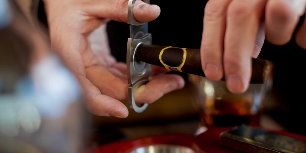 Men's hands cut a cigar with scissors