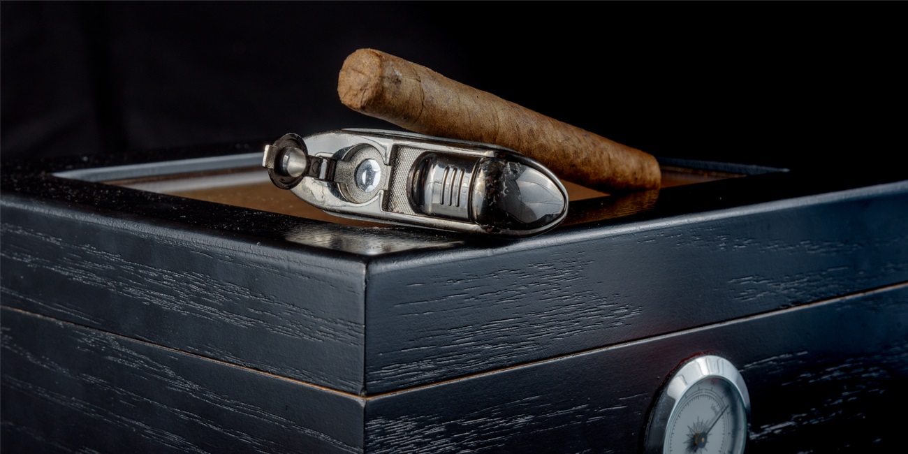 cigar on a black humidor next to a cigar punch torch